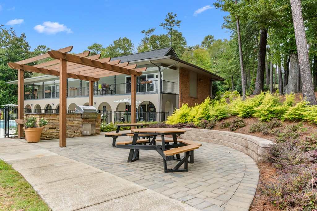A wooden pergola is attached to a building with a patio table and chairs.