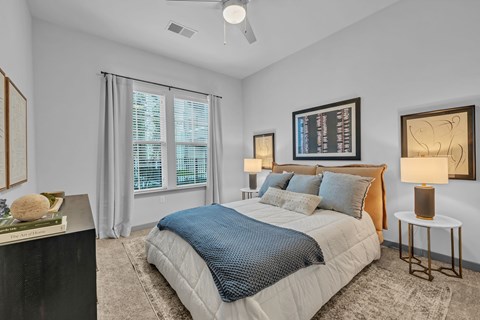 A bedroom with a large bed, a ceiling fan, and a window with blinds.