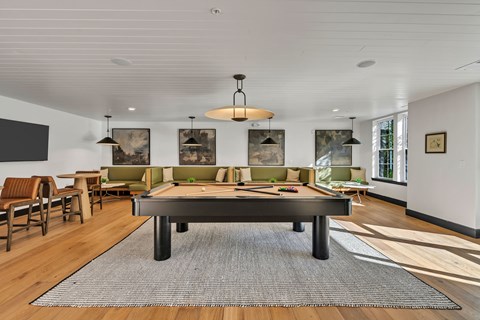 A large, dark pool table is the centerpiece of a spacious room with a light-colored ceiling and a rug in front of it.