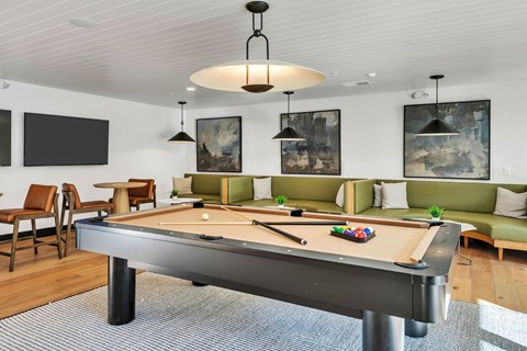 A pool table is in the middle of a room with a green couch and a TV mounted on the wall.