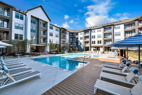 A pool area with sun loungers and apartment buildings in the background.