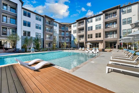 A large swimming pool with lounge chairs is surrounded by apartment buildings.