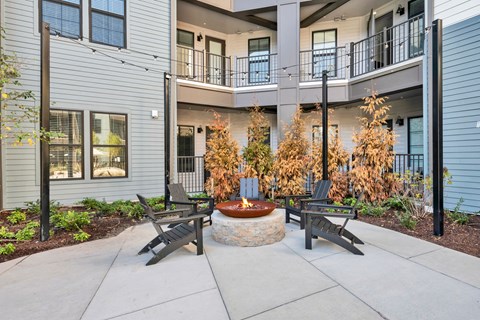 A patio with a fire pit and chairs in front of a building.