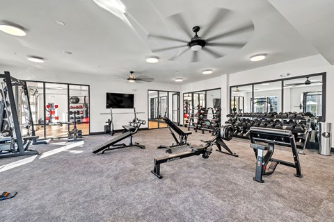 A spacious gym with a variety of equipment and a ceiling fan.