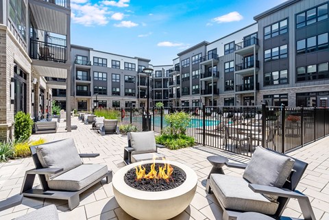 A patio with a fire pit and chairs is surrounded by apartment buildings.