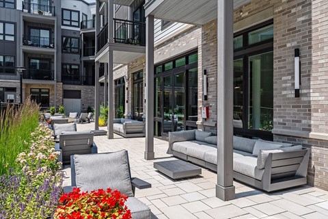 A patio area with grey furniture and a brick building in the background.