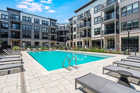 A swimming pool surrounded by sun loungers and apartment buildings.