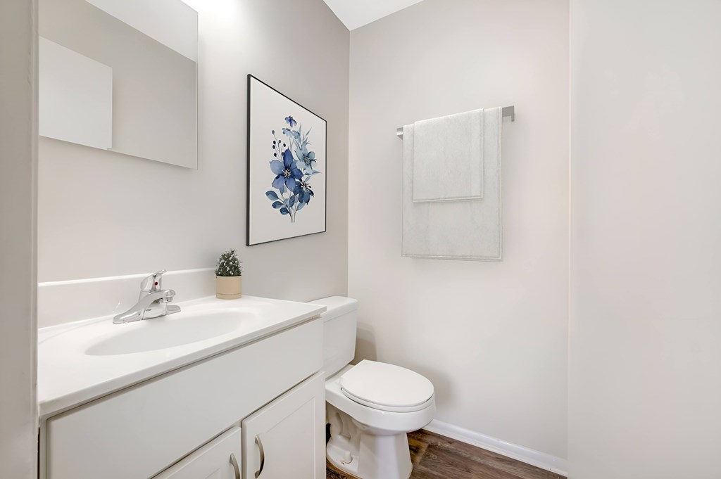 A white bathroom with a toilet, sink, and a picture on the wall.