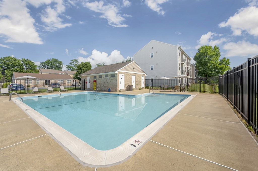 A large outdoor swimming pool surrounded by a concrete patio and a black fence.