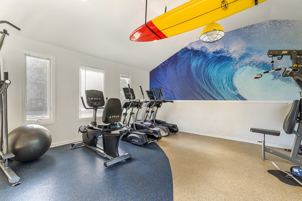 a gym with exercise machines and a surfboard on the wall at Quail Ridge, Plainsboro Township, 08536