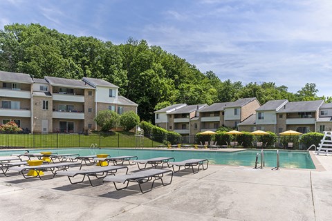 A swimming pool surrounded by lounge chairs in front of apartment buildings.