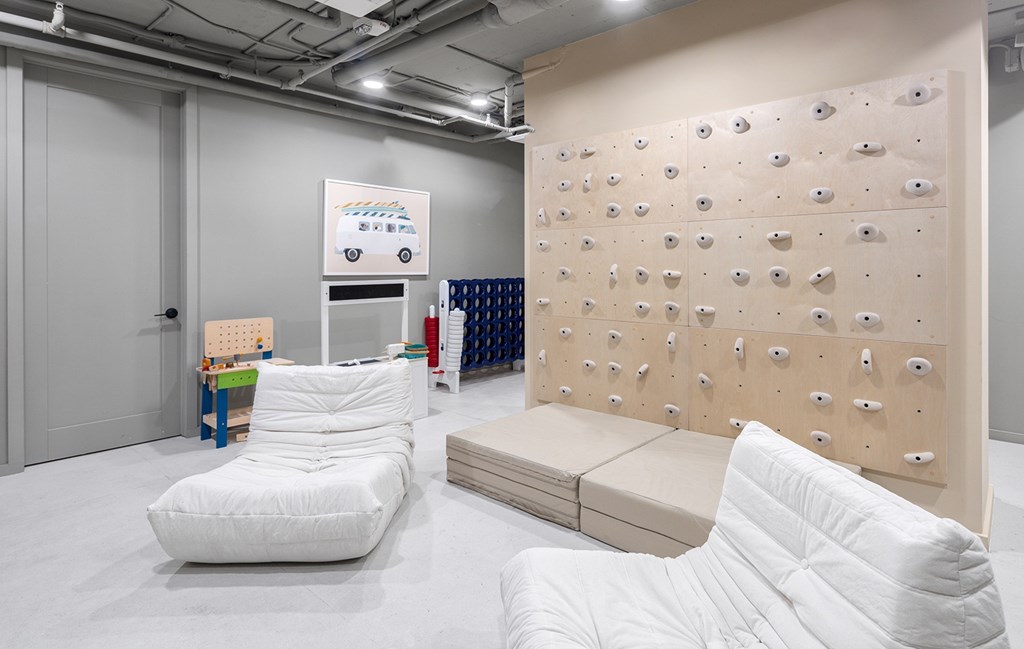 A white chair sits in front of a climbing wall in a room with white walls and floors.