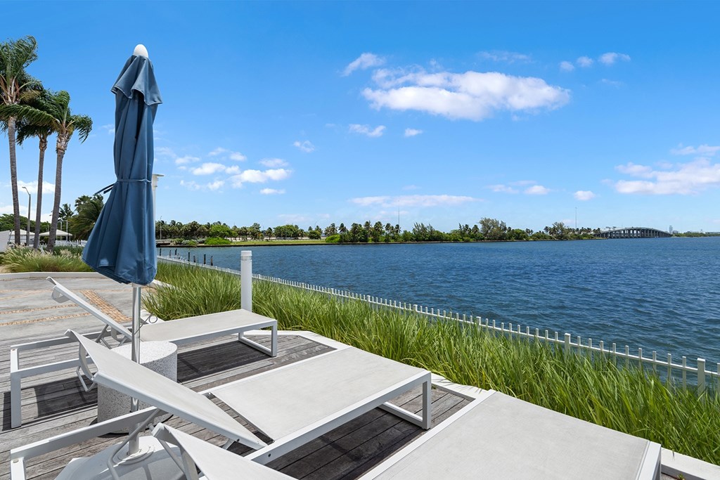 A blue umbrella is on a white chair on a patio overlooking a body of water.