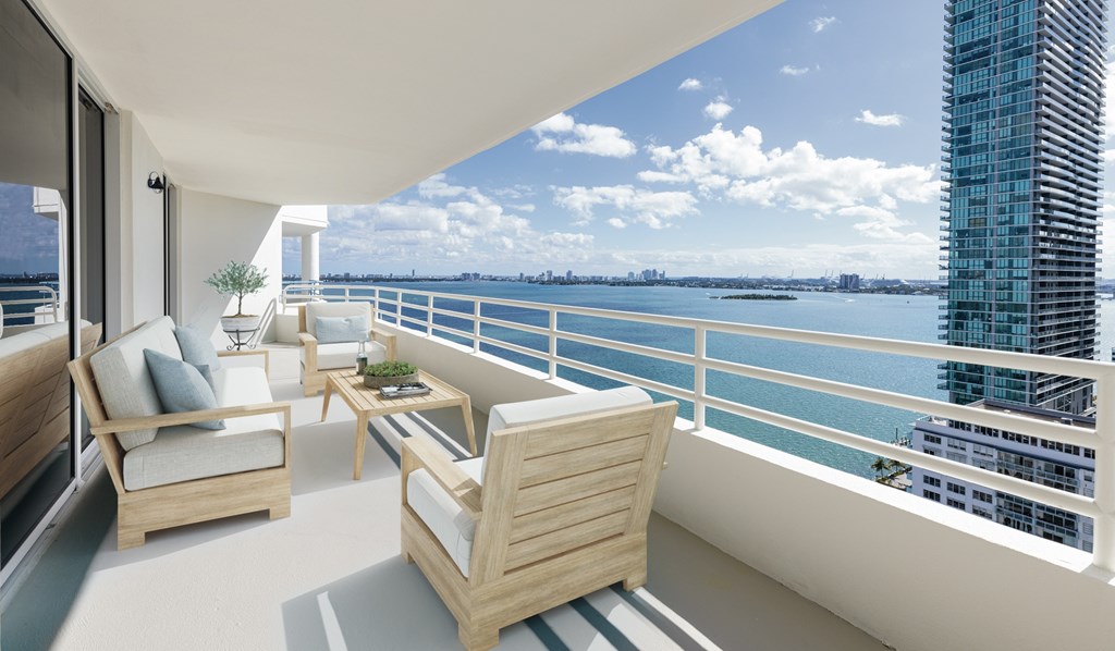 A balcony with a couch, chairs and a table with a view of the water and buildings.