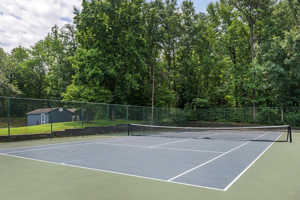a tennis court with a house and trees in the background
