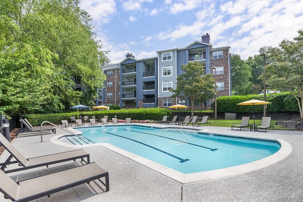 a swimming pool with chairs and umbrellas in front of an apartment building