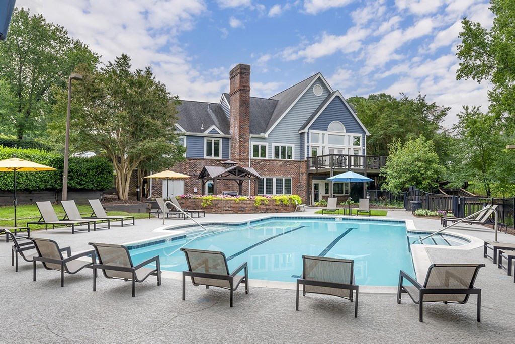 a swimming pool with chairs and a house in the background