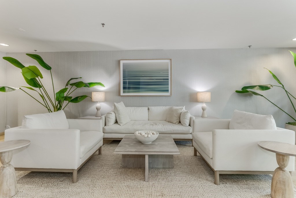 A modern living room with white furniture and a large painting on the wall.
