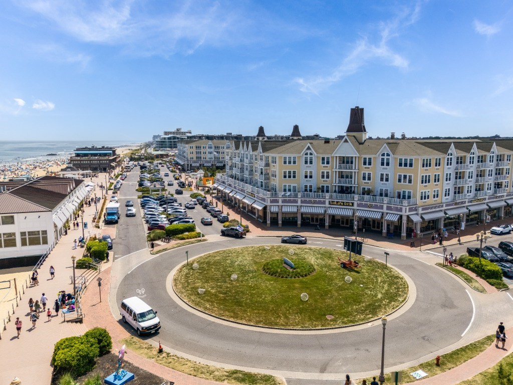 A roundabout with a grassy island in the middle is surrounded by buildings and cars.