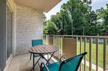 A patio with a table and chairs overlooking a tennis court.