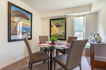 A dining room with a table set for two and a painting of a beach scene on the wall.