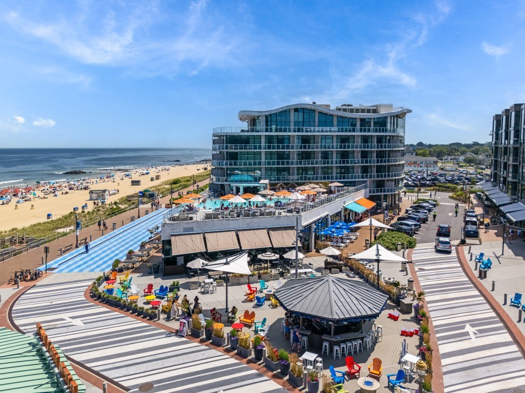 A beachside view with a large building, a gazebo, and people enjoying the sunny day.
