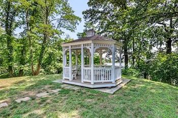 A white gazebo is situated in a grassy area with trees in the background.