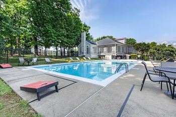 A pool with a bench and chairs in front of a house.