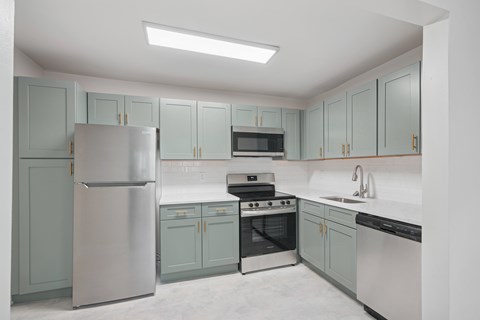 A kitchen with a refrigerator, oven, microwave, and sink.