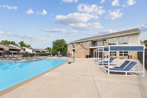 A swimming pool with sun loungers and a building in the background.