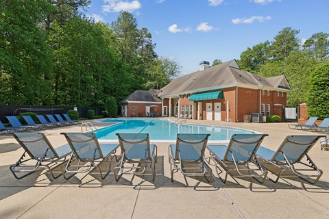 A pool surrounded by lawn chairs in front of a house.