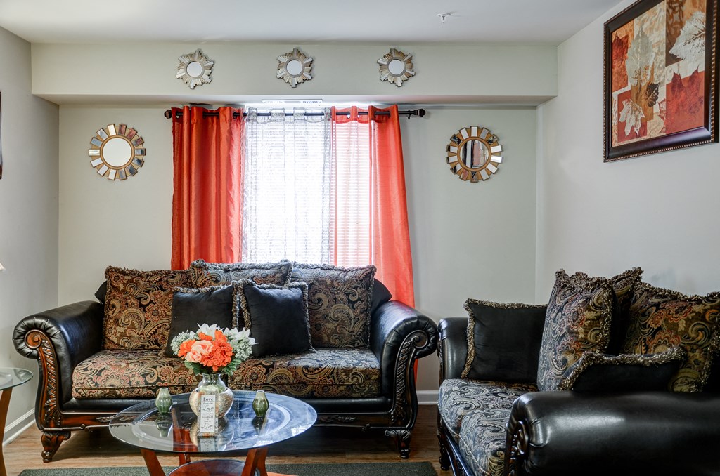a living room with black leather furniture and orange curtains