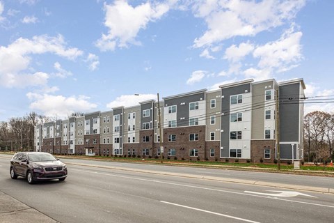 A car is driving on a road in front of apartment buildings.