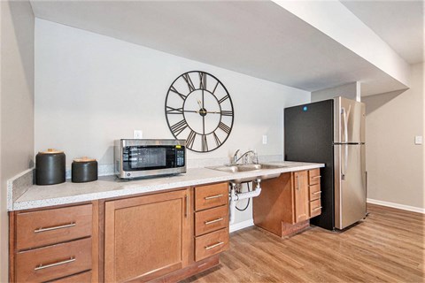 A kitchen with a clock on the wall and a microwave on the counter.