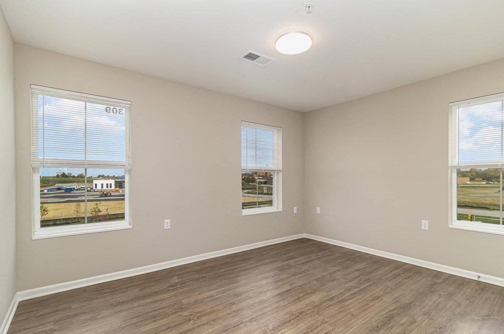 an empty living room with wood flooring and two windows