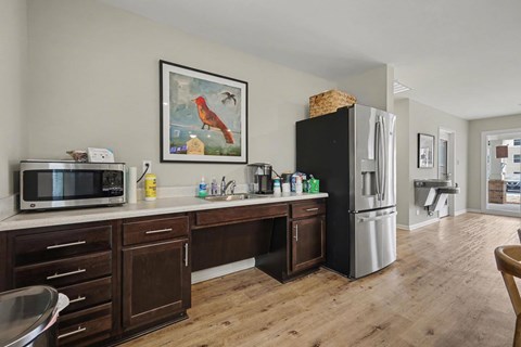 A kitchen with a black fridge, wooden cabinets, and a painting of a rooster on the wall.