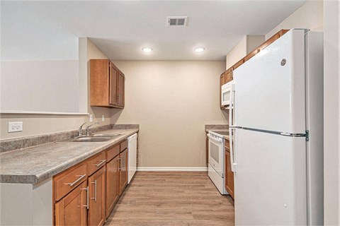 A kitchen with a white refrigerator, brown cabinets, and a marble countertop.