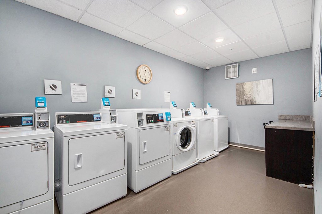 a laundromat with a row of washers and dryers and a clock
