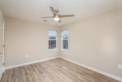 Empty room with a ceiling fan and two windows.