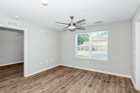 A room with a ceiling fan and a window showing a view of a street.