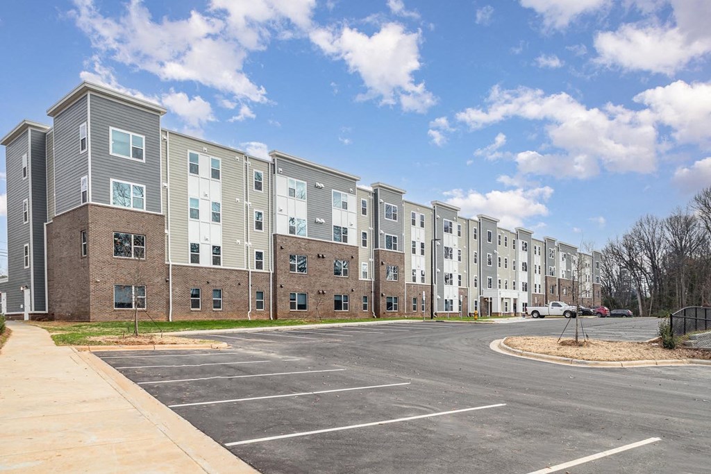 A row of modern apartment buildings with a parking lot in front.
