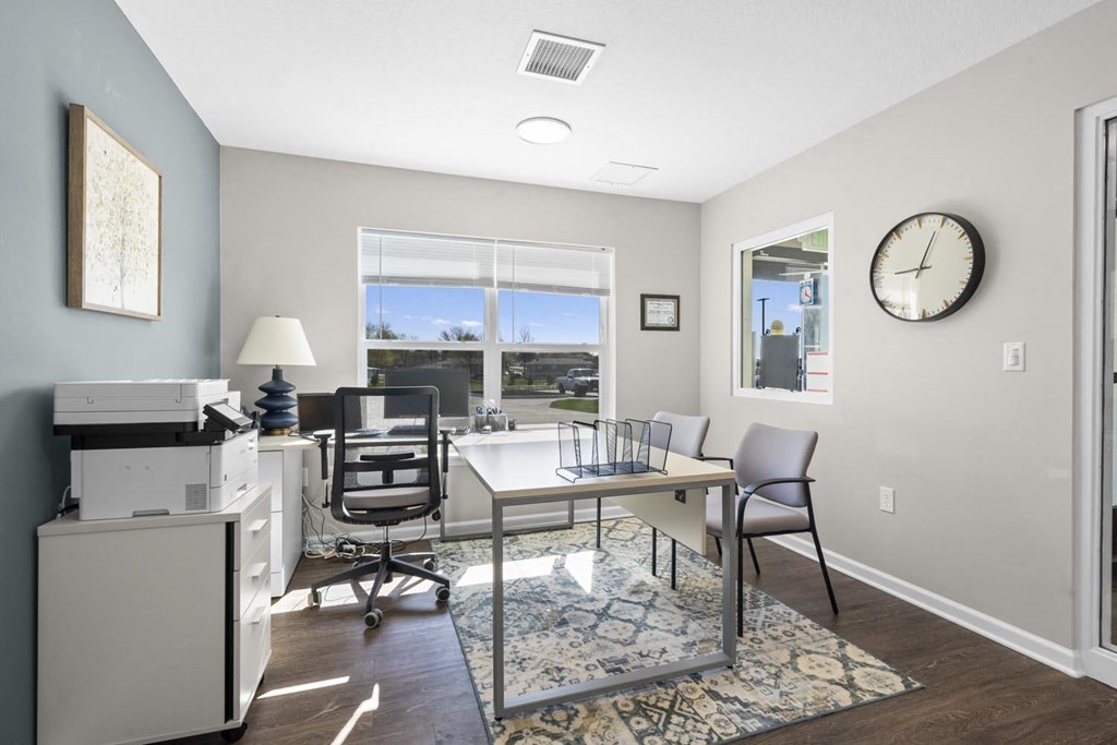 a desk with a computer and a printer in a room with a large window