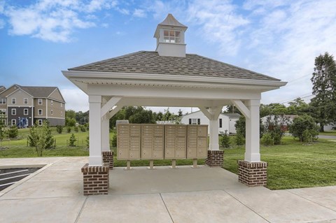 A gazebo with a clock tower is surrounded by a brick wall and a grassy area.