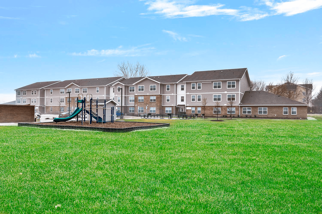 a playground in the grass in front of an apartment building