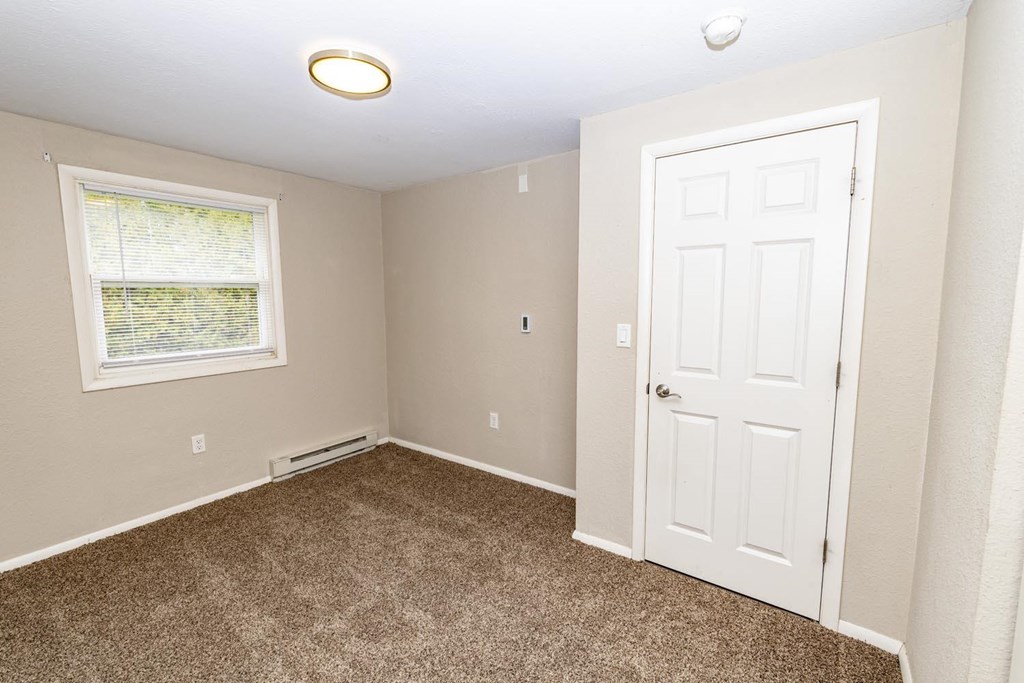 A room with a carpeted floor, a window with blinds, a door, and a ceiling light fixture.