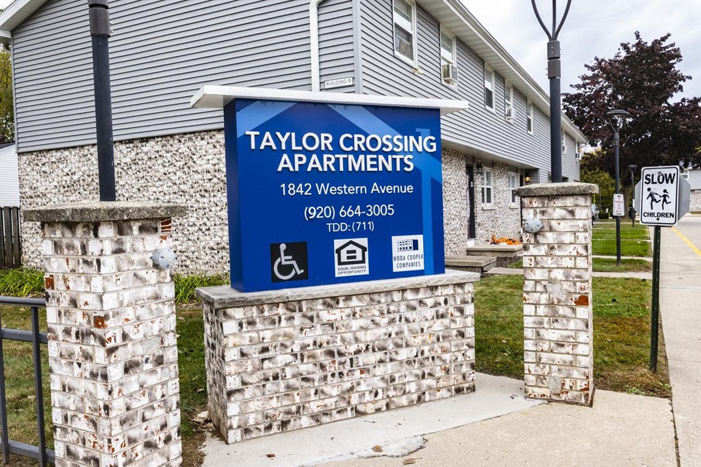 A sign for Taylor Crossing Apartments is displayed in front of a building.