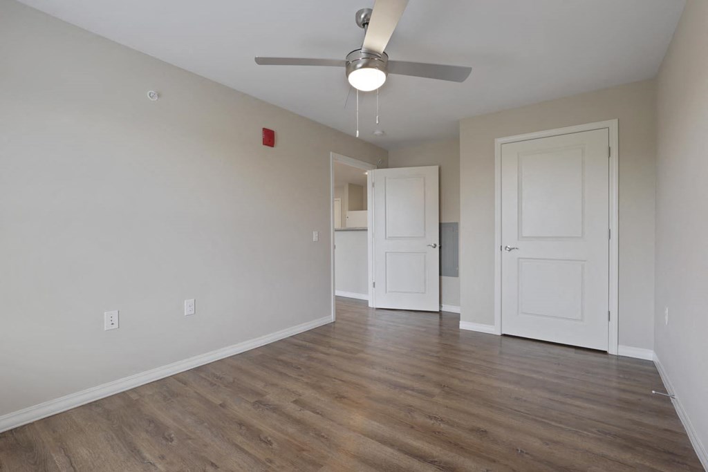 an empty living room with a ceiling fan and a door to the kitchen