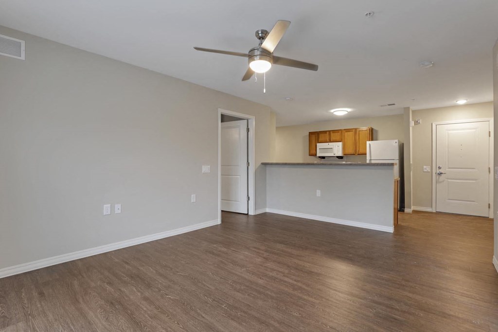 an empty living room with a ceiling fan and a kitchen