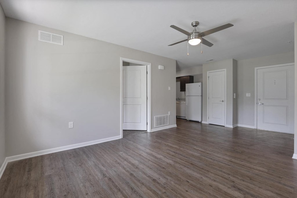 an empty living room with a ceiling fan and a kitchen