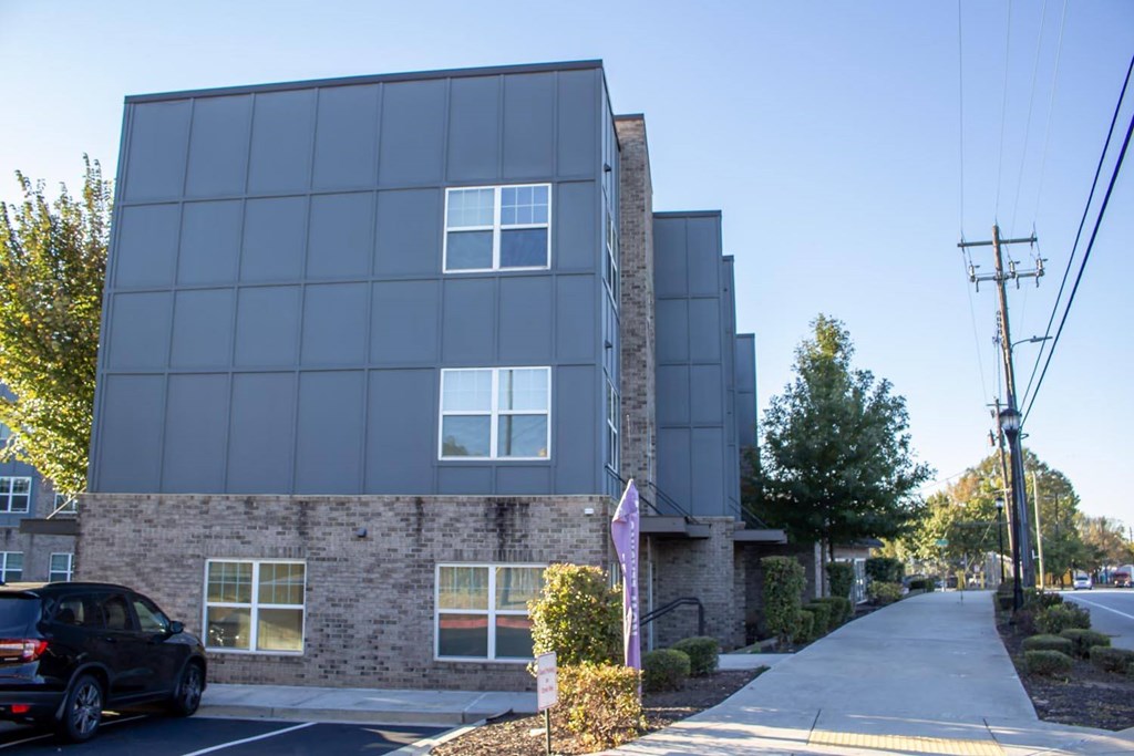A modern building with a glass facade is situated on a street with a sidewalk and a parked car.